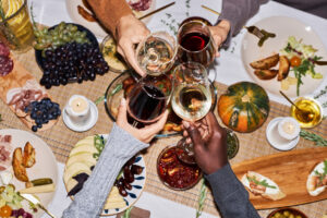 Top view of people toasting with wine glasses at festive dinner table celebrating Thanksgiving, copy space